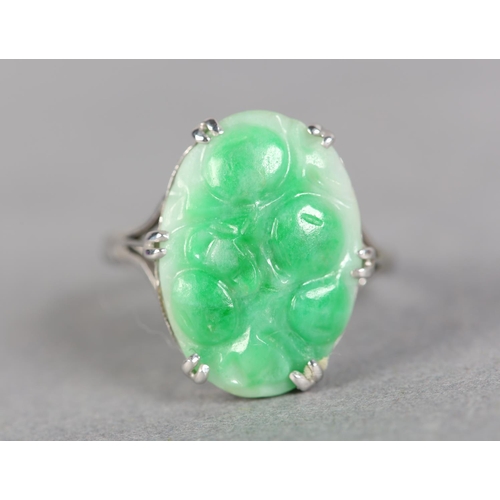 242 - A JADE DRESS RING c.1960, the oval peach carved cabochon claw set flanked by trifoil shoulders in wh... 