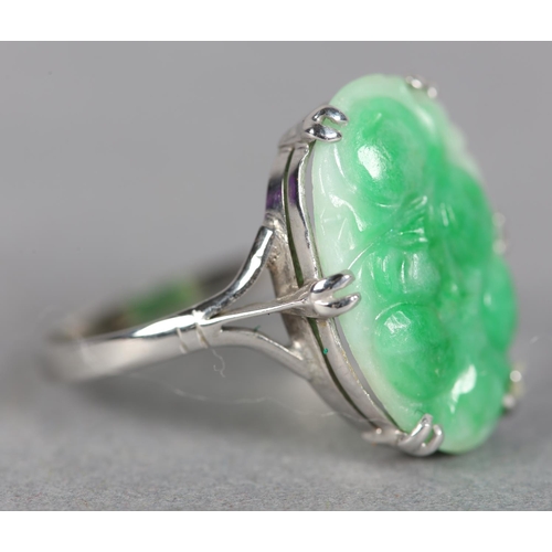 242 - A JADE DRESS RING c.1960, the oval peach carved cabochon claw set flanked by trifoil shoulders in wh... 