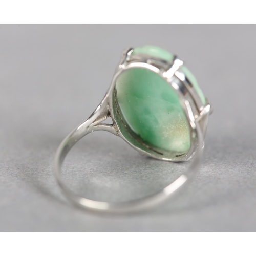 242 - A JADE DRESS RING c.1960, the oval peach carved cabochon claw set flanked by trifoil shoulders in wh... 