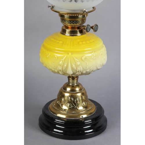 98 - A VICTORIAN BRASS OIL LAMP embossed with a band of plant forms, having a yellow tinted glass reservo... 