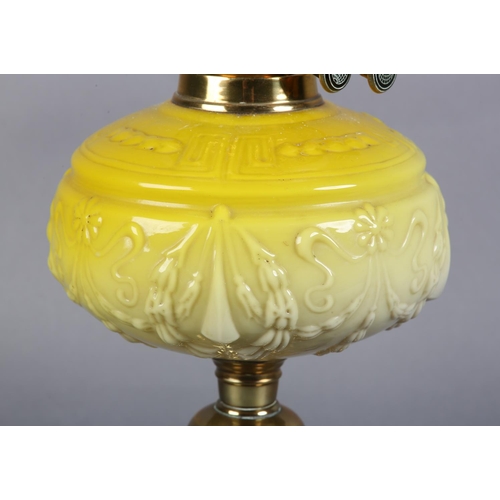 98 - A VICTORIAN BRASS OIL LAMP embossed with a band of plant forms, having a yellow tinted glass reservo... 