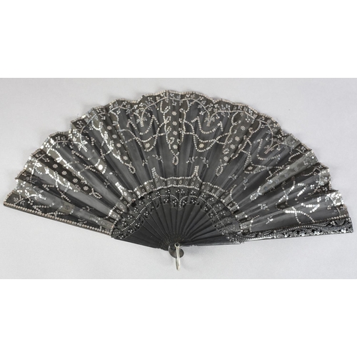 37 - C 1905/10, a wood fan with incised and clouté monture, the black gauze leaf applied with silk panels... 