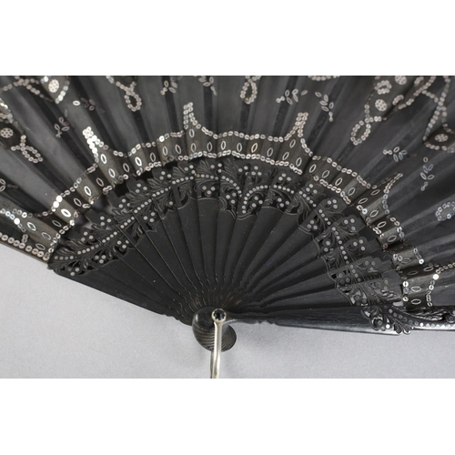 37 - C 1905/10, a wood fan with incised and clouté monture, the black gauze leaf applied with silk panels... 