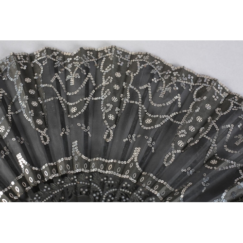 37 - C 1905/10, a wood fan with incised and clouté monture, the black gauze leaf applied with silk panels... 