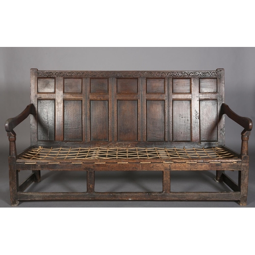 377 - AN 18TH CENTURY OAK SETTLE, the back having seven field panels, strung seat with later cushion, slab... 