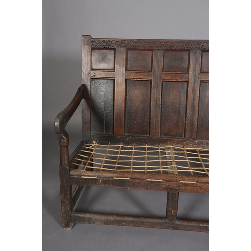 377 - AN 18TH CENTURY OAK SETTLE, the back having seven field panels, strung seat with later cushion, slab... 