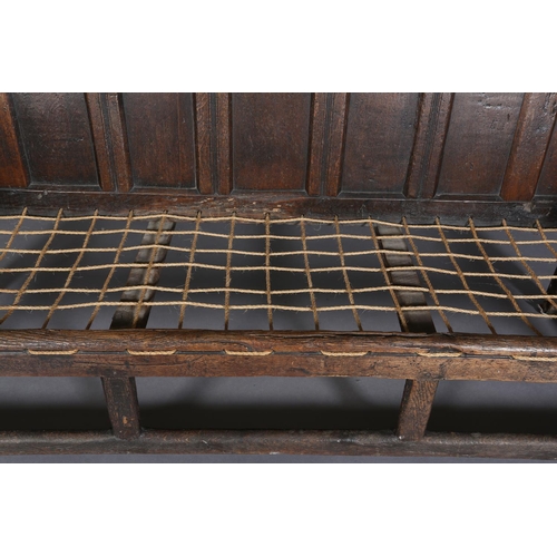 377 - AN 18TH CENTURY OAK SETTLE, the back having seven field panels, strung seat with later cushion, slab... 