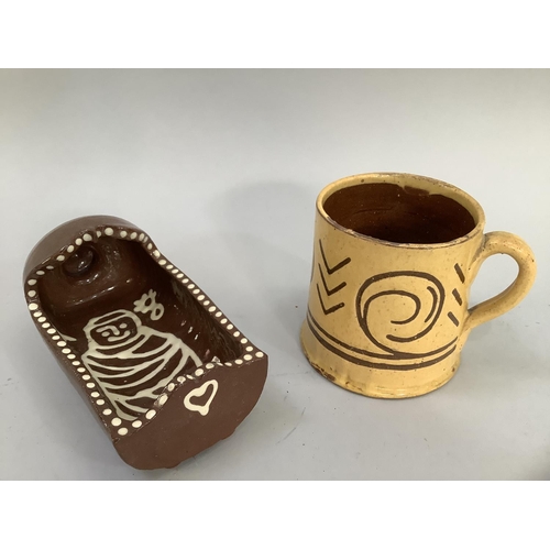 11 - A slipware cradle, 18cm long and an earlier earthenware mug, the yellow glaze incised with geometric... 