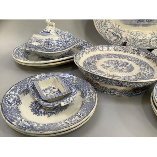 16 - A quantity of blue and white printed dinner ware with figures in a boat beside a cottage within a bo... 