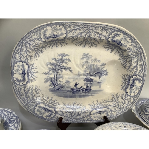 16 - A quantity of blue and white printed dinner ware with figures in a boat beside a cottage within a bo... 