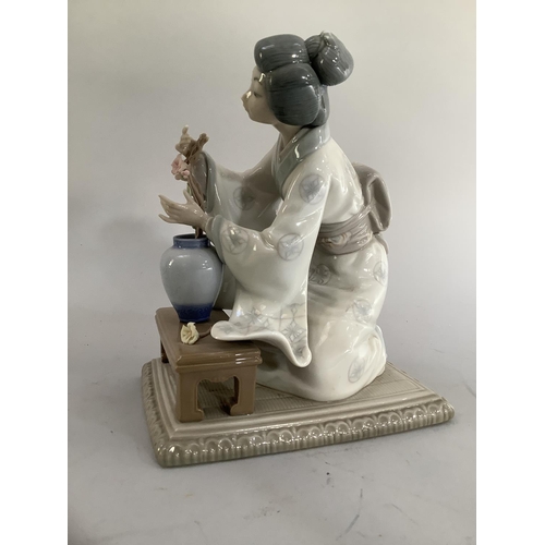 21 - A Lladro figure of a Japanese bijin arranging flowers in a vase on rectangular base, 19cm approximat... 