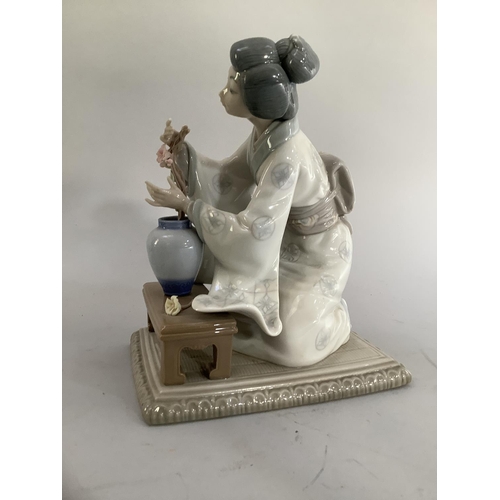 21 - A Lladro figure of a Japanese bijin arranging flowers in a vase on rectangular base, 19cm approximat... 