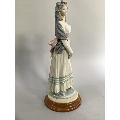 22 - A Lladro figure of a young woman wearing a mantilla, her dress with a ribboned sash to the waist and... 