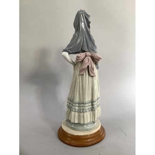 22 - A Lladro figure of a young woman wearing a mantilla, her dress with a ribboned sash to the waist and... 