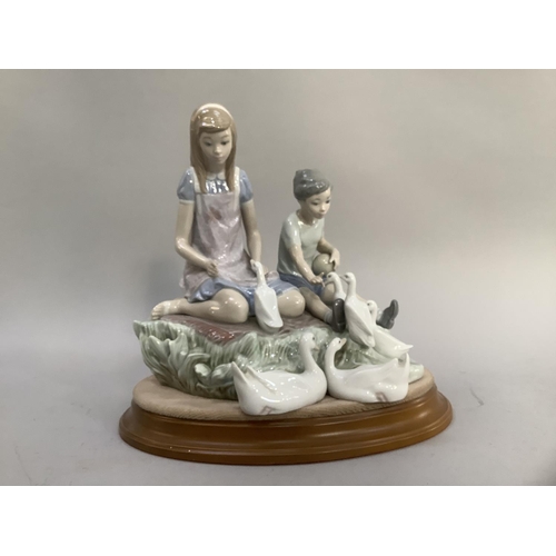 24 - A large Lladro figure group of young girl and boy sitting on a grassy bank feeding ducks with oval p... 