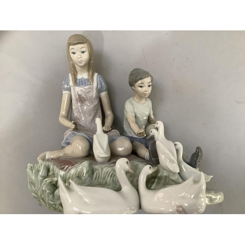 24 - A large Lladro figure group of young girl and boy sitting on a grassy bank feeding ducks with oval p... 