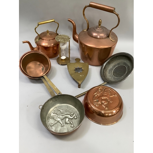 91 - A collection of copperware comprising two copper kettles, two moulds, pans, a brass trivet etc