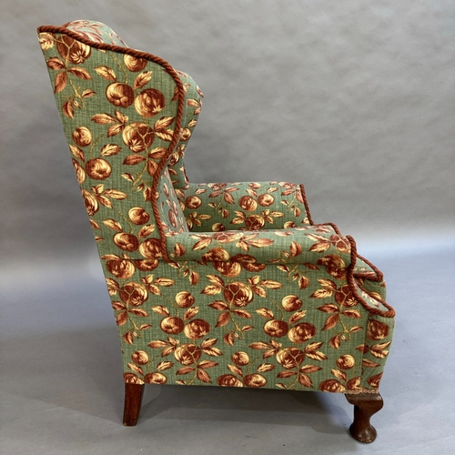 347 - A 1930s wing backed armchair reupholstered in fabric of deep pink and cream fruit on a pale green gr... 