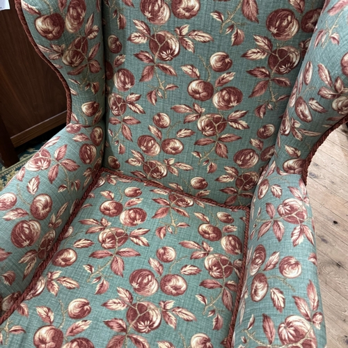 347 - A 1930s wing backed armchair reupholstered in fabric of deep pink and cream fruit on a pale green gr... 