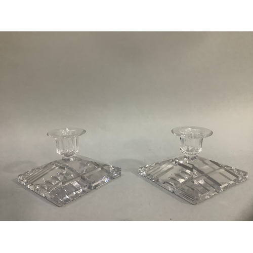 54 - A pair of cut glass candlesticks, having flat rims and faceted sockets, on a square canted bases cut... 