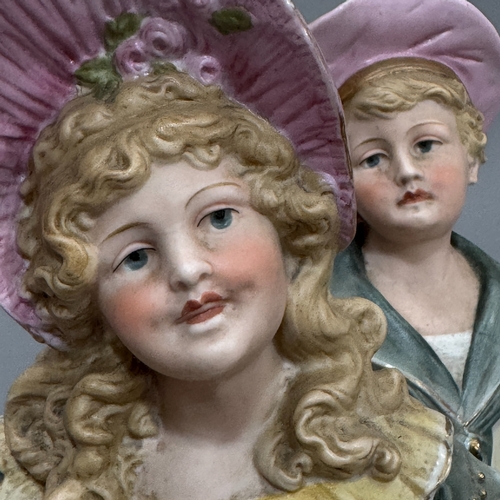 15 - A pair of late Victorian bisque figures, a girl and boy standing beside bocage, 38cm approximately