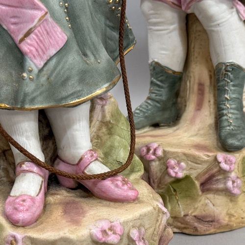 15 - A pair of late Victorian bisque figures, a girl and boy standing beside bocage, 38cm approximately