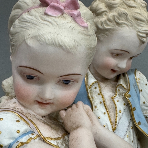 16 - A pair of late 19th century German bisque figures of a young boy and girl, each with a posy basket b... 