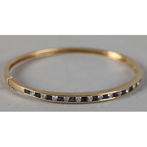 208 - A SAPPHIRE AND DIAMOND STIFF HINGED BANGLE in 18ct gold, the brilliant cut diamonds and calibre cut ... 