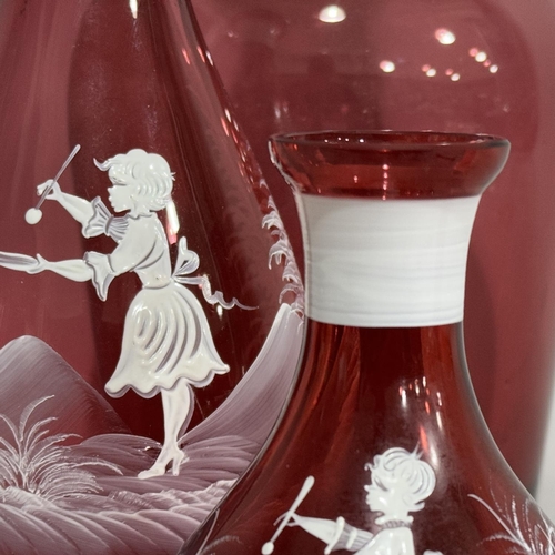 54B - An oversized cranberry glass decanter, 31cm high together with two Mary Gregory style cranberry glas... 