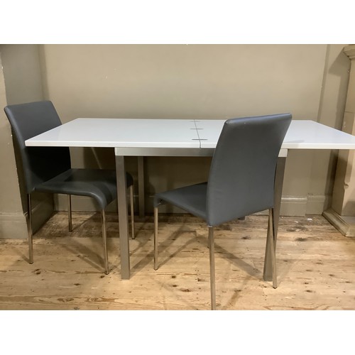 228 - A modern white extending dining table on chrome square legs together with two grey chairs