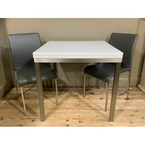 228 - A modern white extending dining table on chrome square legs together with two grey chairs