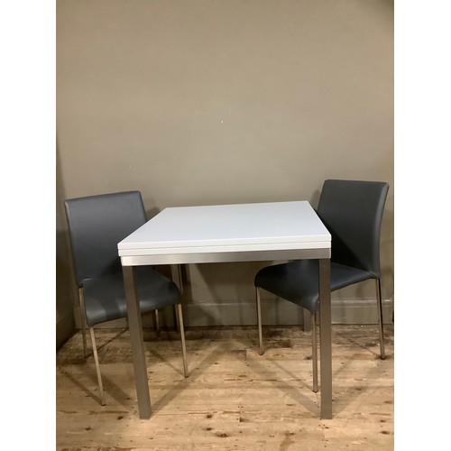 228 - A modern white extending dining table on chrome square legs together with two grey chairs