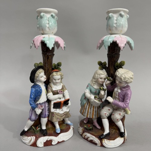 33 - A pair of figural candlesticks modelled as girl and boy reading a book and young couple with basket ... 