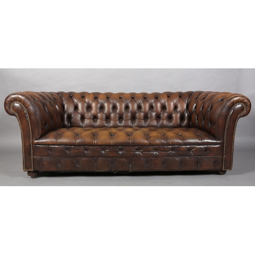 130 - A brown buttoned leather back Chesterfield sofa with close nail studding, on front bun feet with con... 