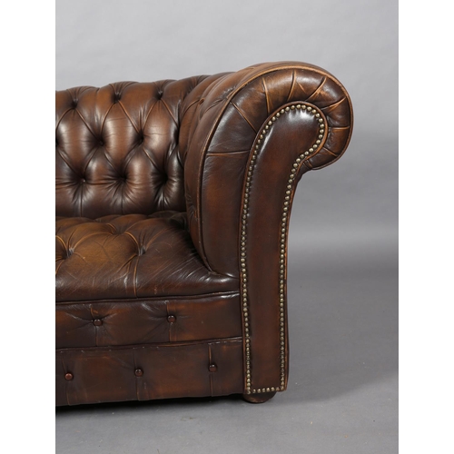 130 - A brown buttoned leather back Chesterfield sofa with close nail studding, on front bun feet with con... 