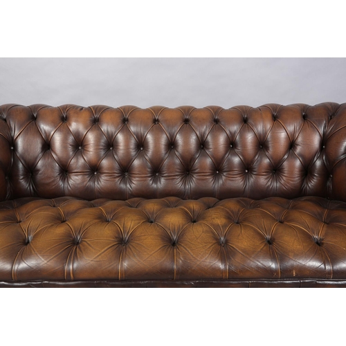 130 - A brown buttoned leather back Chesterfield sofa with close nail studding, on front bun feet with con... 