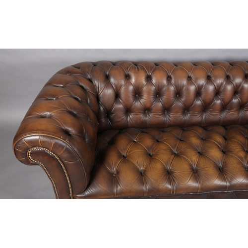 130 - A brown buttoned leather back Chesterfield sofa with close nail studding, on front bun feet with con... 