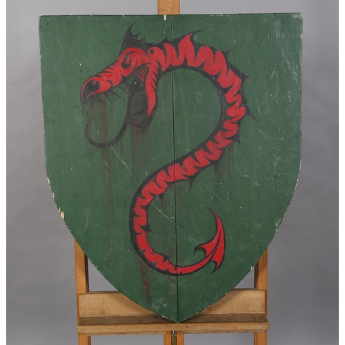 164 - A shield shaped wooden plaque painted with a red dragon on a green ground, 74cm x 63cm