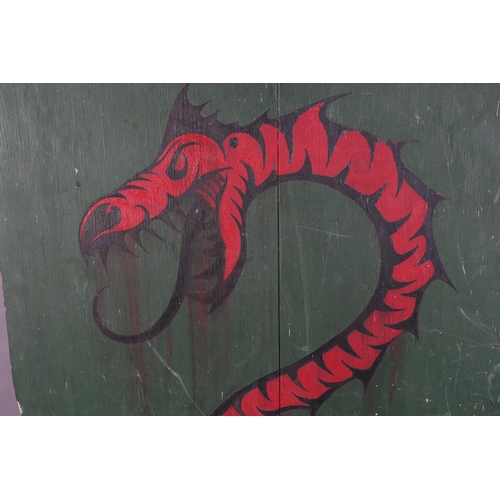 164 - A shield shaped wooden plaque painted with a red dragon on a green ground, 74cm x 63cm