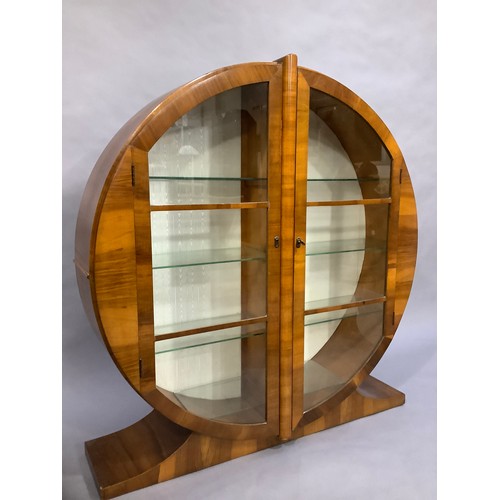 38 - An Art Deco walnut display cabinet of circular outline and two doors, on platform feet, the interior... 