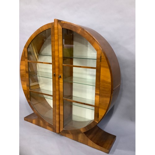 38 - An Art Deco walnut display cabinet of circular outline and two doors, on platform feet, the interior... 