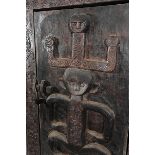 110 - An African inspired dark wood single door cupboard, having a wavy pediment, carved with two birds ab... 