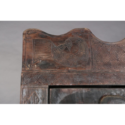 110 - An African inspired dark wood single door cupboard, having a wavy pediment, carved with two birds ab... 