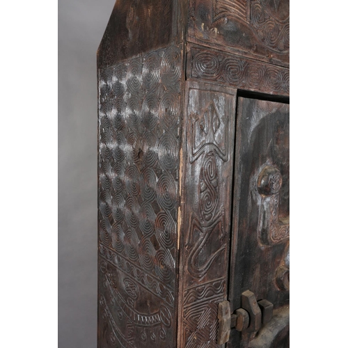 110 - An African inspired dark wood single door cupboard, having a wavy pediment, carved with two birds ab... 