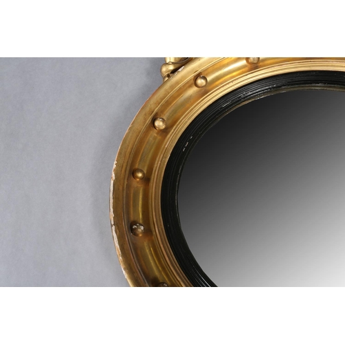 284 - A REGENCY GILT WOOD AND GESSO CONVEX WALL MIRROR, the circular frame applied with spheres and surmou... 