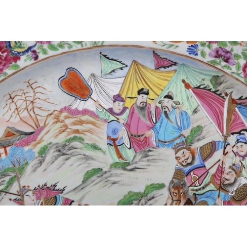 124 - A CHINESE CANTON FAMILLE ROSE CHARGER of oval outline, enamelled with a battle scene, warriors on ho... 