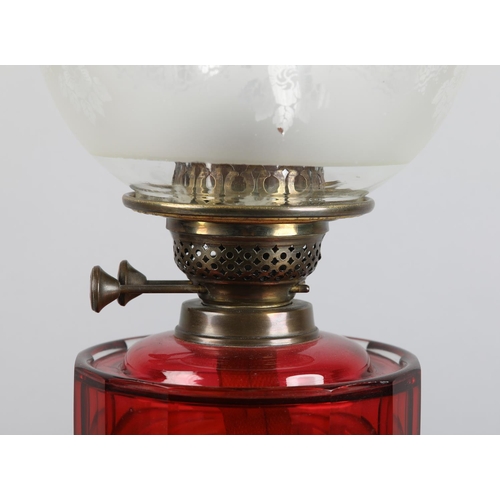 23 - A VICTORIAN BRASS OIL LAMP, having an etched globe shade, cranberry panelled glass reservoir, on cir... 