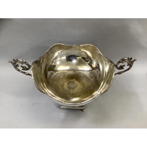 16 - A silver plated two handled punch bowl having a wavy rim and dragon head handles on a reeded and flu... 