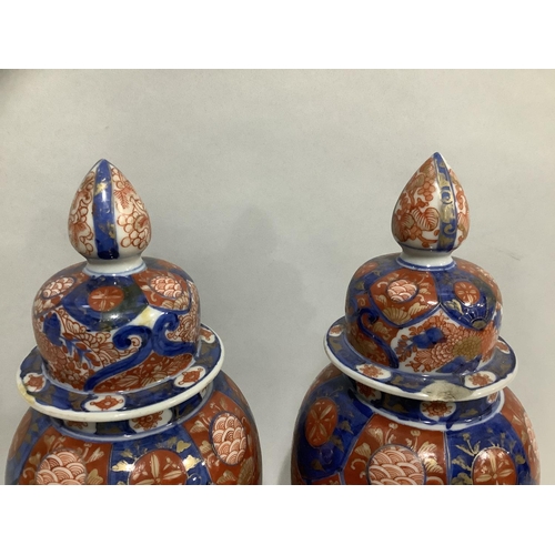 14 - A pair of Imari vases and domed covers with bud finials, overall height on stand 30cm