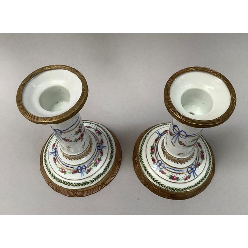 20 - A pair of French porcelain and gilt metal mounted candlesticks, hand painted with ribboned swags of ... 
